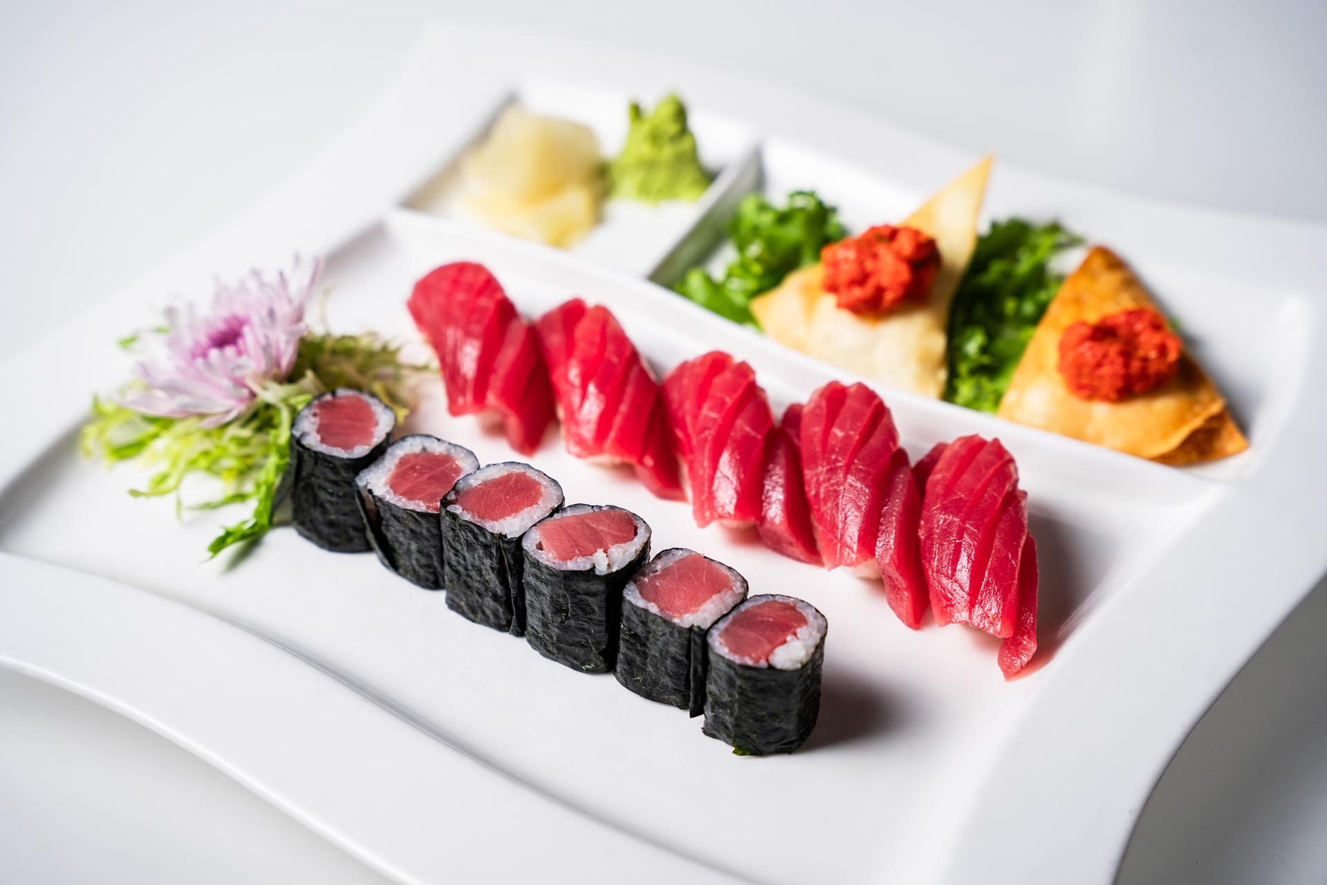 Tuna sushi and tuna rolls served on a white plate with garnishes