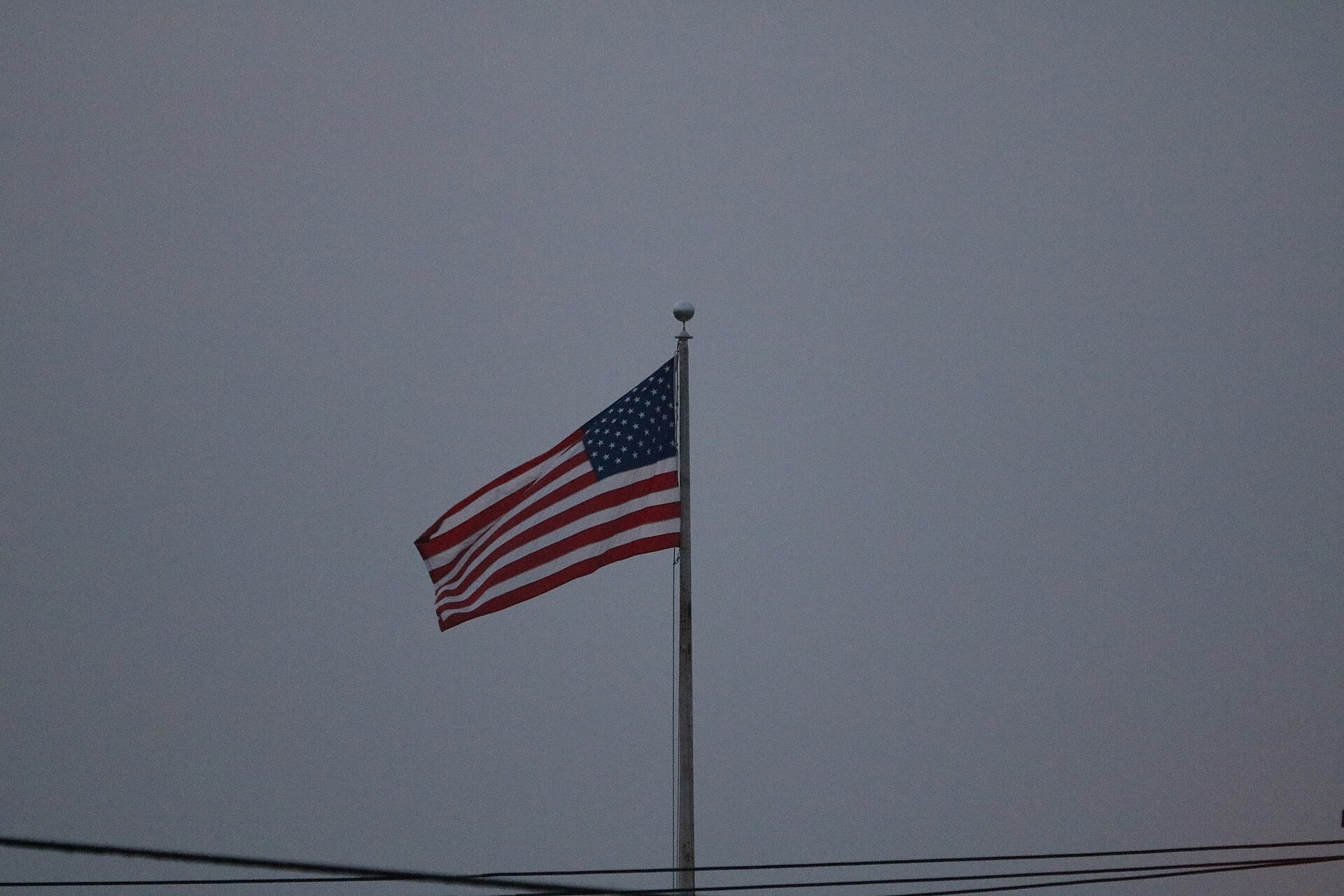 An American flag waving on a tall flagpole against a pale sky