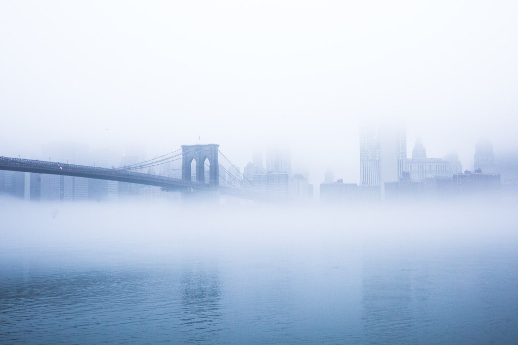 Brooklyn Bridge and the Manhattan skyline rising out of morning fog at sunrise