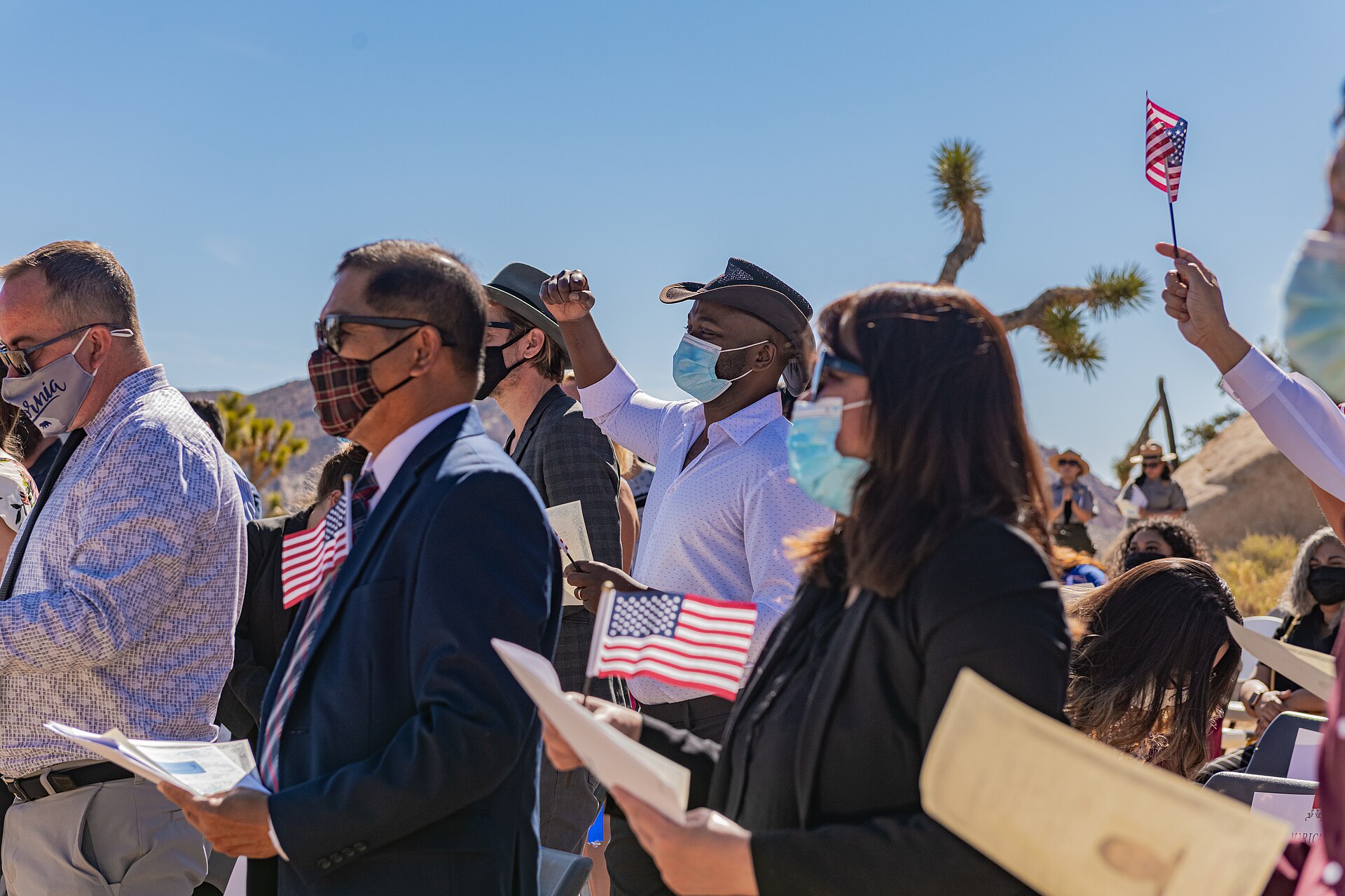New citizens at an outdoor naturalization ceremony holding small American flags and certificates