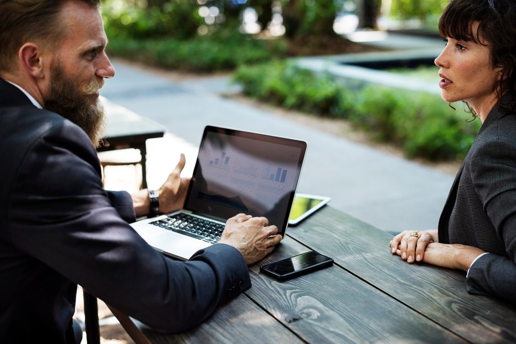 A mentor walks an entrepreneur through business growth charts on a laptop during an outdoor meeting